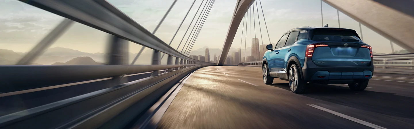 a rear view of a blue 2026 Nissan Kicks crossing a bridge