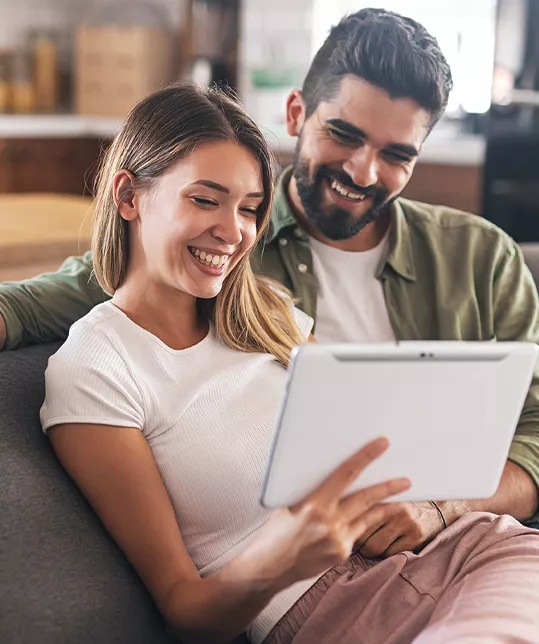 husband and wife looking at a tablet at home on the couch