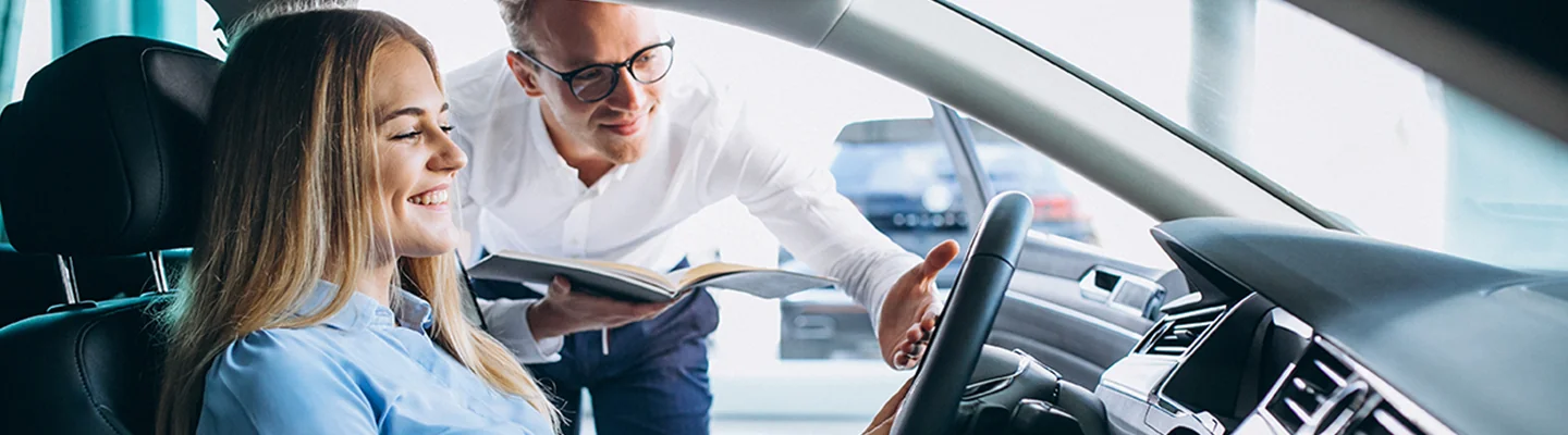 a person seated in car being shown features of the car by salesperson in showroom