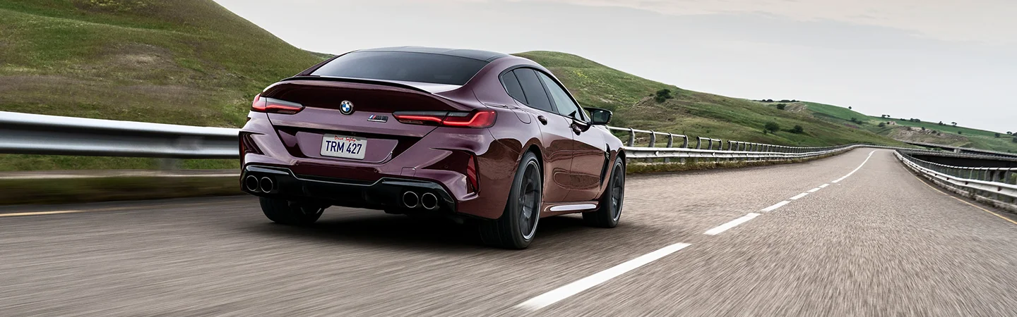 Back view of a 2025 BMW M8 Coupe driving by hills