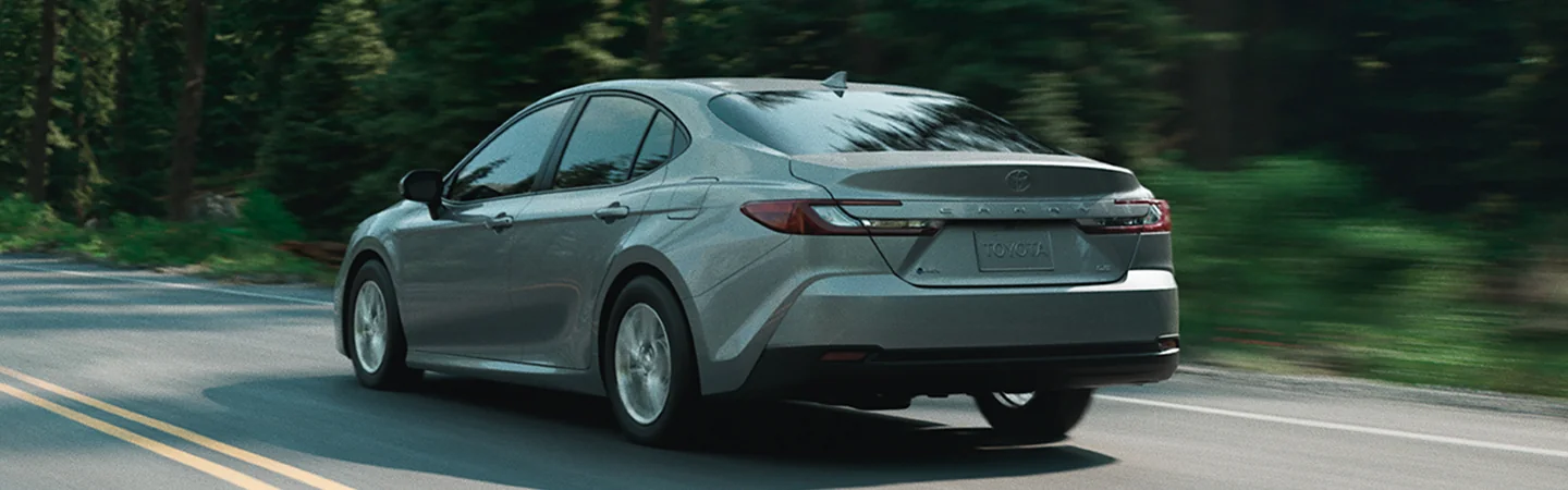 Back side view of a gray 2025 Toyota Camry driving on a road with a forest in the background