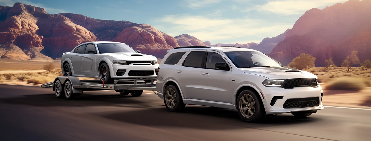 A greay 2026 Dodge Durango pulling a trailer with a Dodge Charger on it in the desert