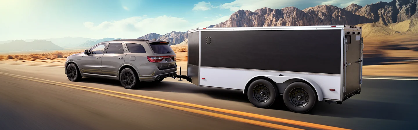 Side view of a gray 2026 Dodge Durango pulling a trailer though the desert