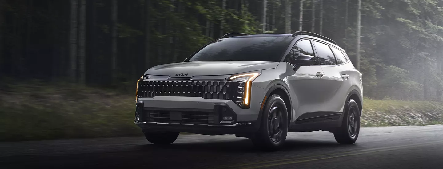 2026 Kia Sportage Hybrid driving on a road with trees and mist in the background