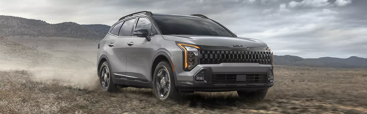 2026 Kia Sportage Hybrid driving on a dirt road with mountains in the background