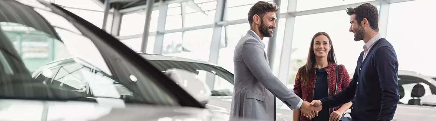Two people shaking hands in front of a parked car