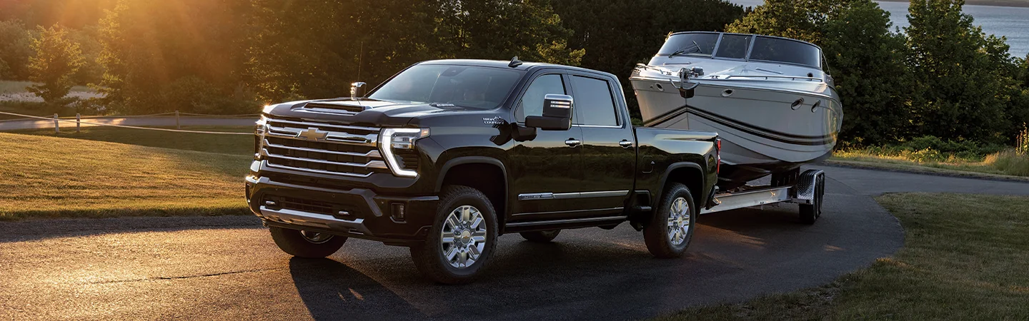 Side view of a black 2026 Chevy Silverado 2500 pulling into a driveway pulling a boat