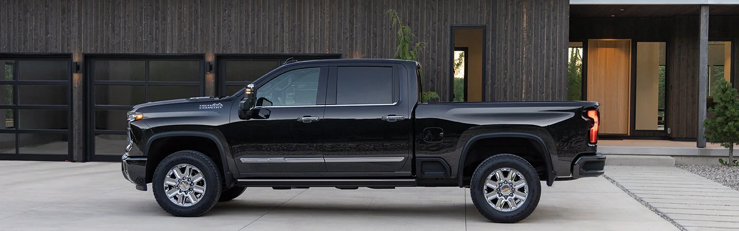 Side view of a parked black 2026 Chevy Silverado 2500in front of a house