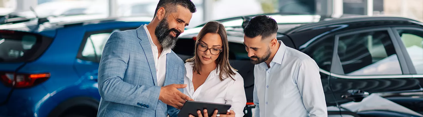 salesman, saleswoman and office admin looking over information on a table with the vehicles behind them