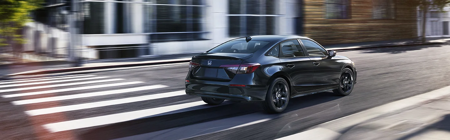Back view of a black 2026 Honda Civic Hybrid driving in the city