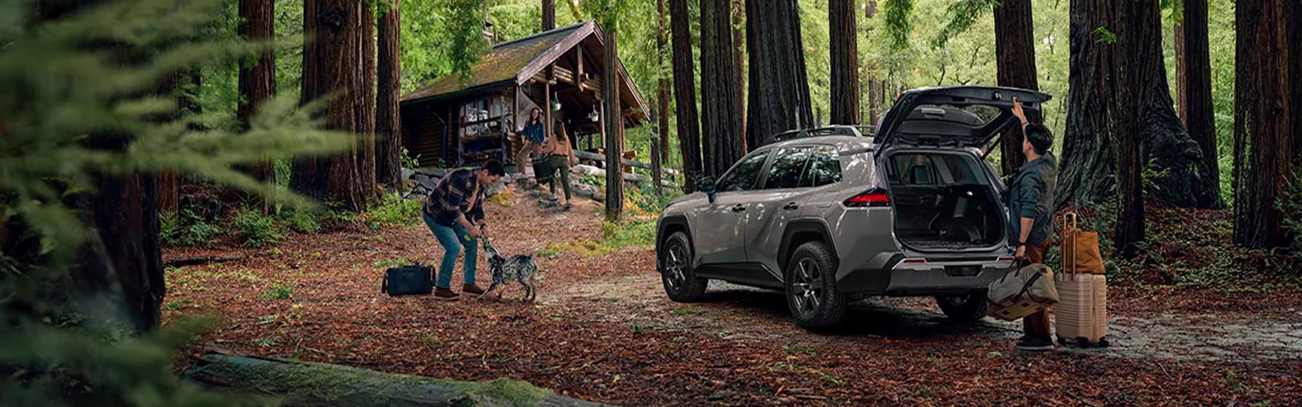 2026 Toyota RAV4 parked outside of a cabin in the woods with a family taking lugagge out of the trunk