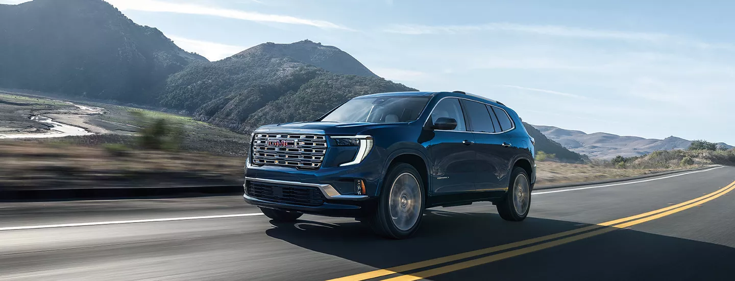 2026 GMC Acadia driving on a road with mountains in the background