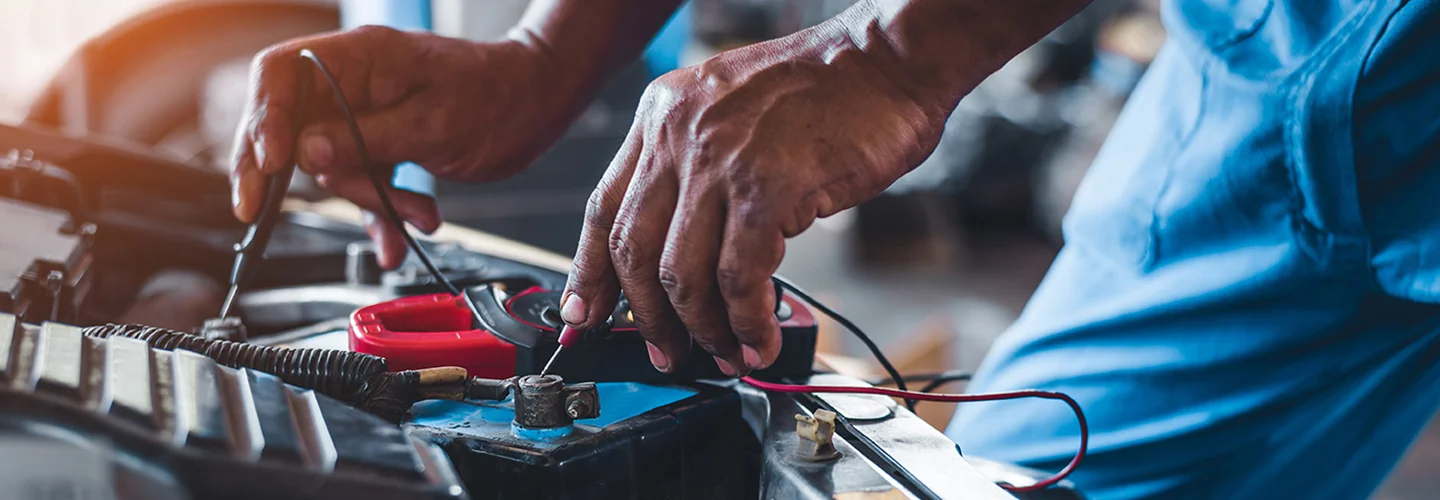 auto mechanic testing battery with voltage meter