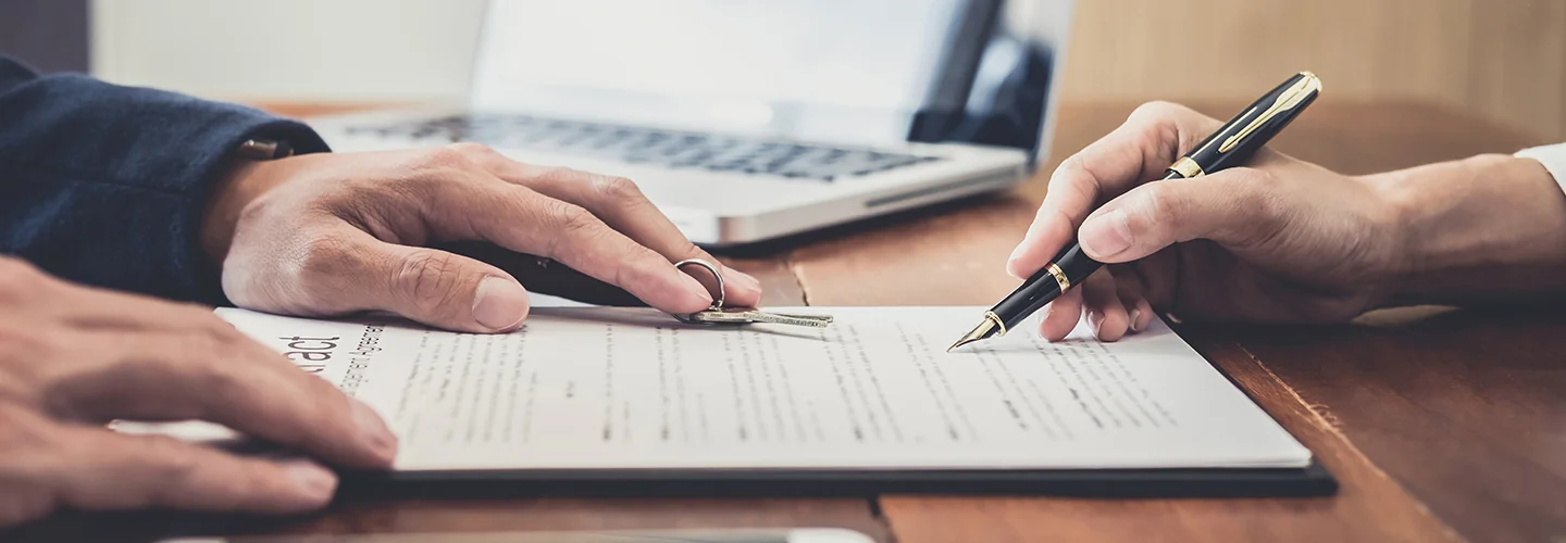 image of two hands one with pen over a contract