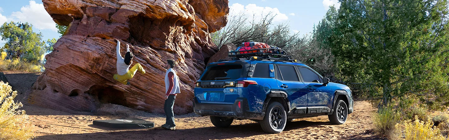 2026 Subaru Outback Wilderness parked by rocks with climbers hanging on to side