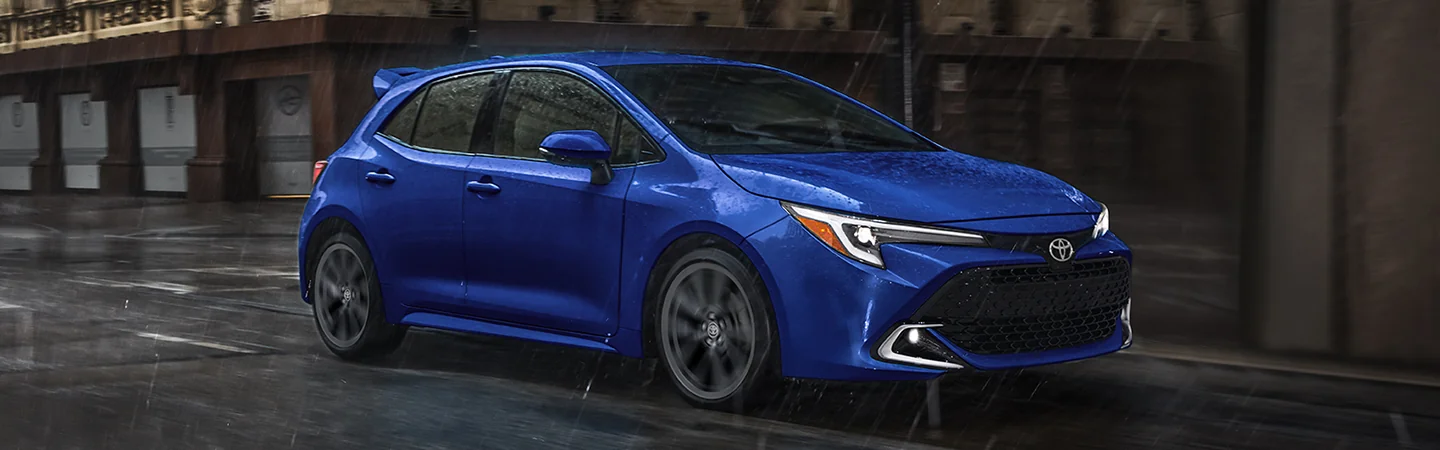 a blue 2025 Toyota Corolla Hatchback driving though a city in the rain