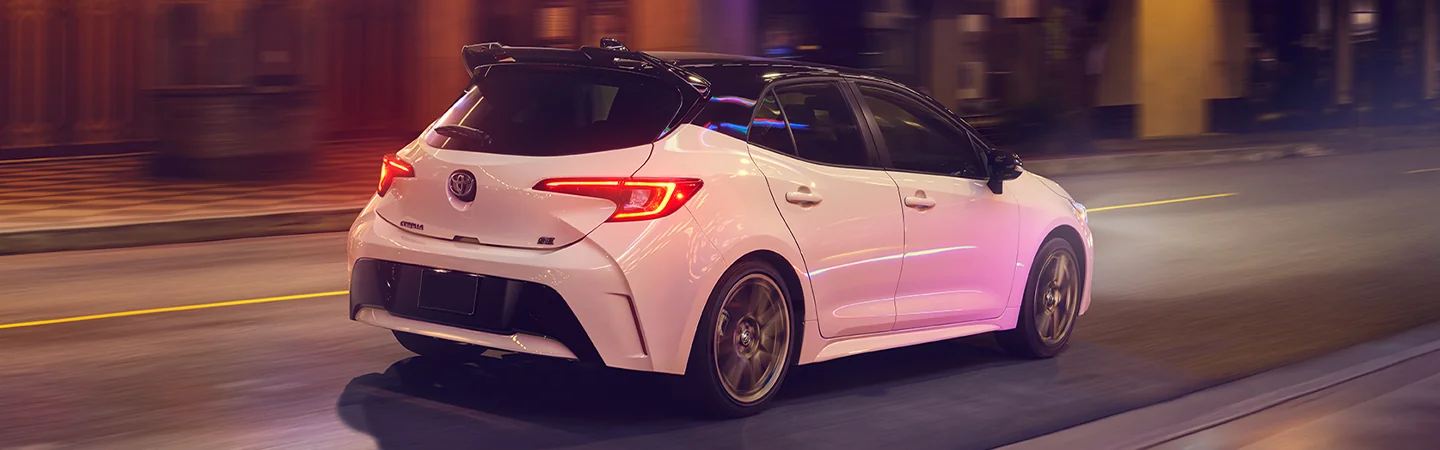 Back side view of a white 2025 Toyota Corolla Hatchback driving in the city