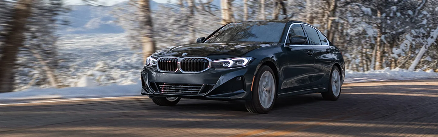 Front view of a black 2026 BMW 3 Series driving on a snowy road