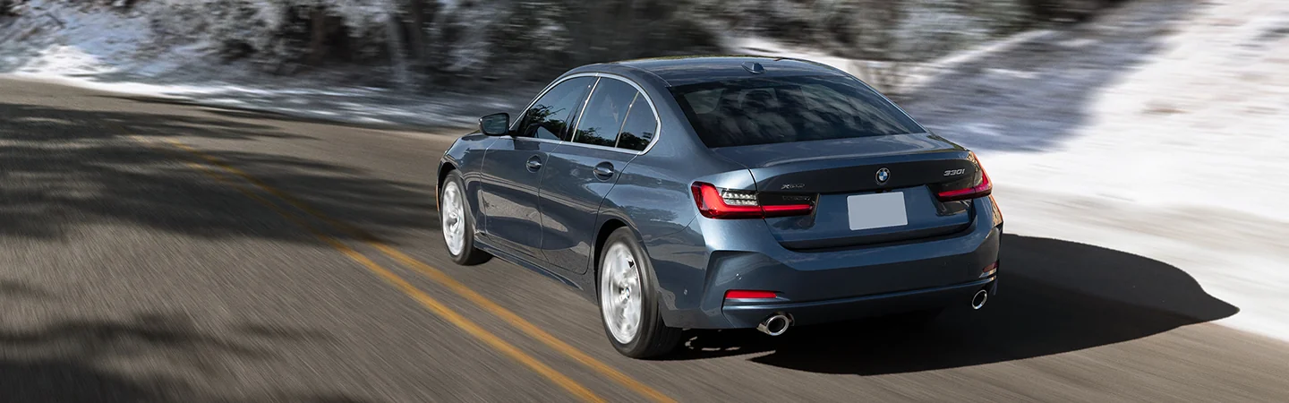 Back view of a blue 2026 BMW 3 Series driving on a snowy road
