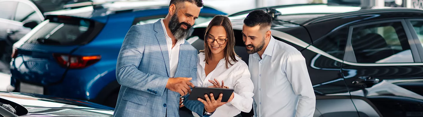 salesman showing a couple information on a table with the vehicles around