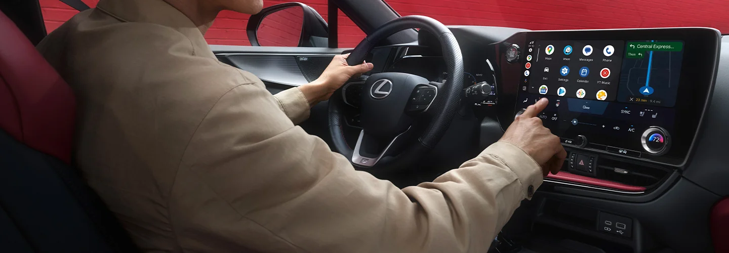 Interior view of a person sitting in the driver seat of a 2026 Lexus NX and using the dashboard tech