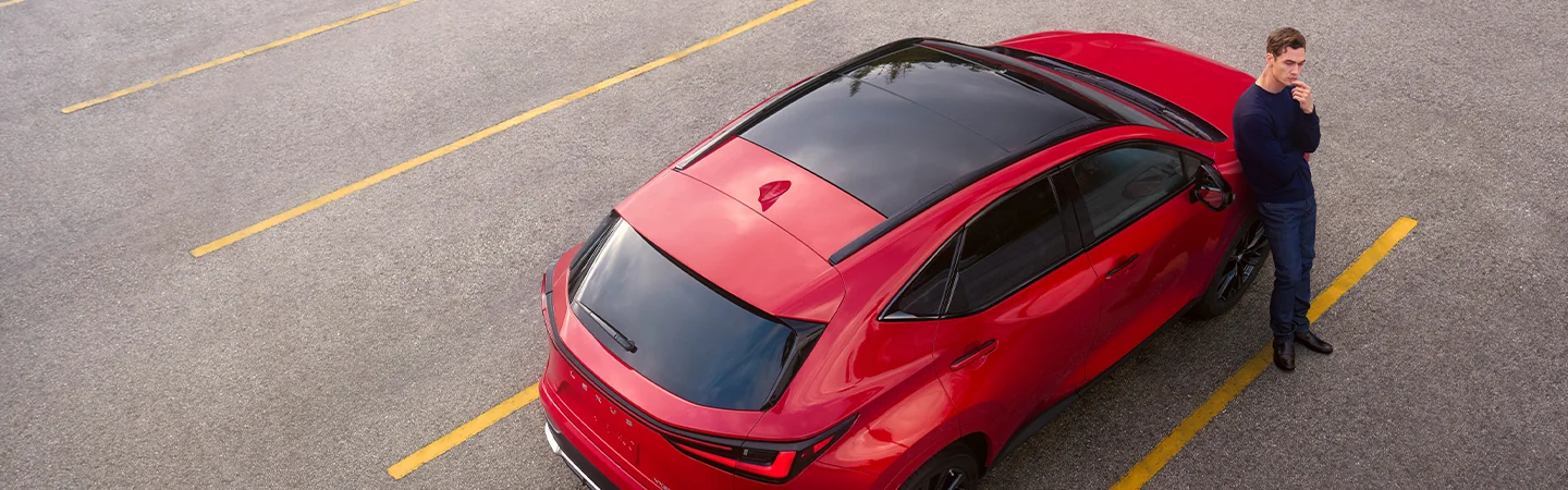 Top view of a parked red 2026 Lexus NX in a parking lot with a man standing next to the car