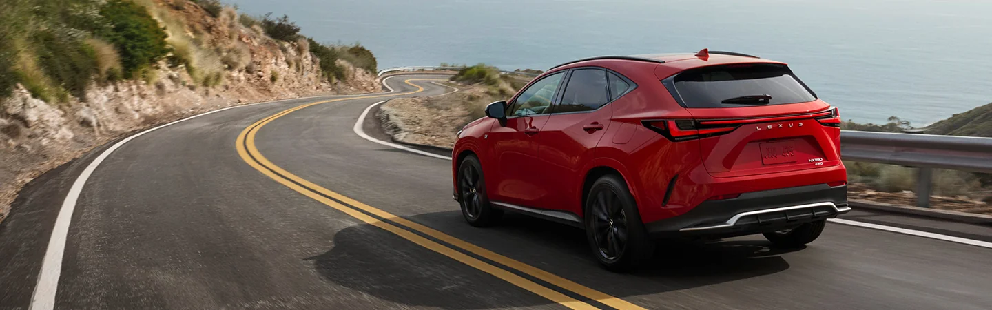 BAck side view of a red 2026 Lexus NX driving on a road next to the ocean