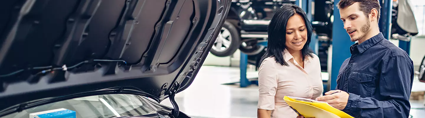 A man and woman stand beside a parked car, smiling and engaged in conversation.