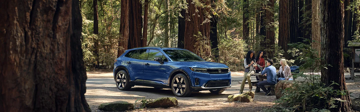 People sitting at a picnic table in the woods with a 2026 Honda Prologue in the background
