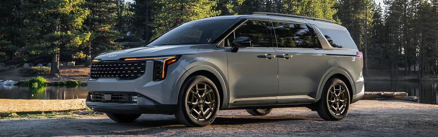 front view of a gray 2026 Kia Carnival parked by a lake