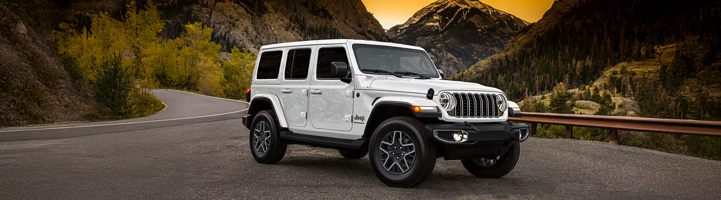 2026 Jeep Wrangler parked in front of mountains with a sunset in the background