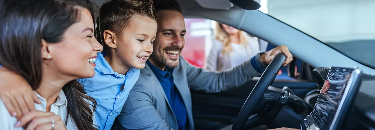 husband, wife and child smiling inside the vehicle looking at the dashboard