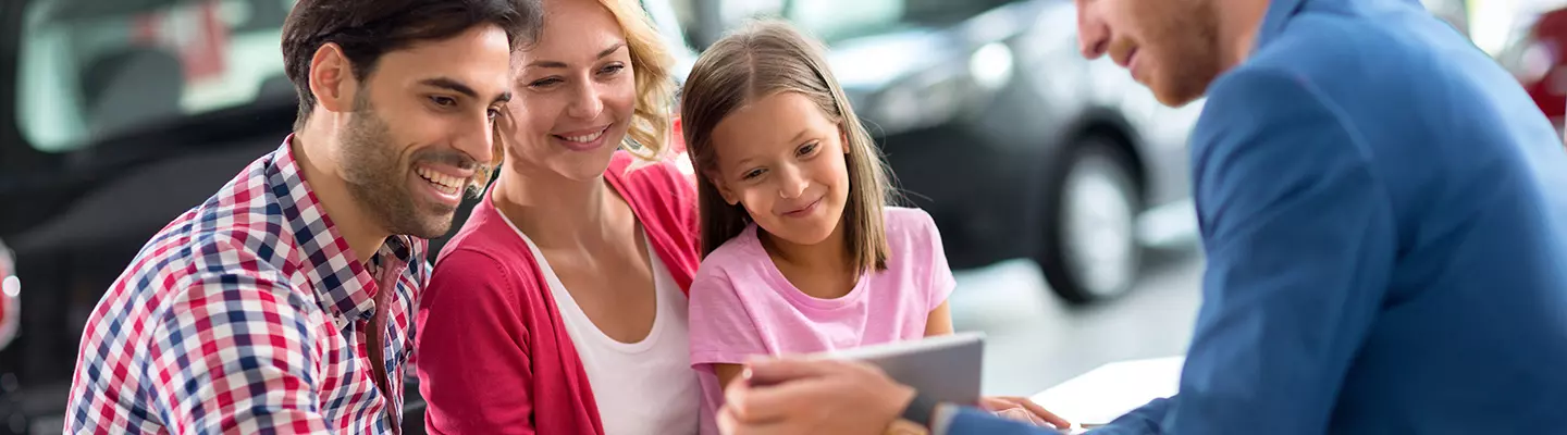 A family examines a car at a dealership, discussing options and features together.