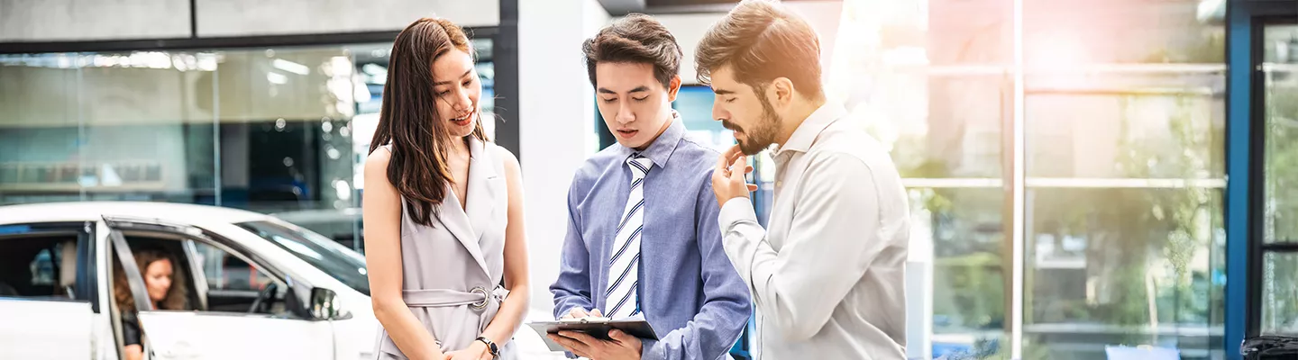 salesman showing man and woman information on a tablet in front of the dealership