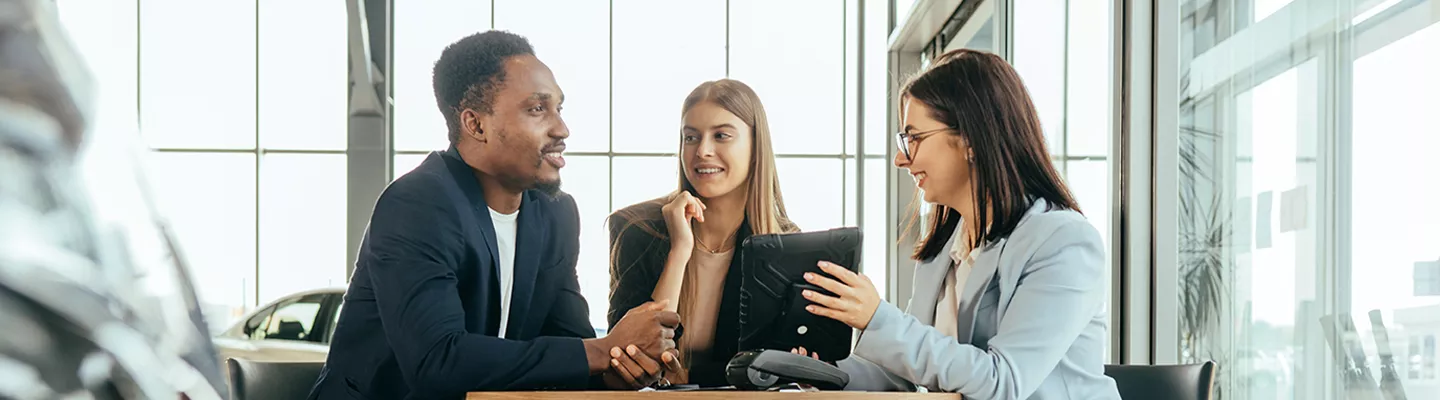 Three people sitting at a table looking at a tablet in a Subaru dealership