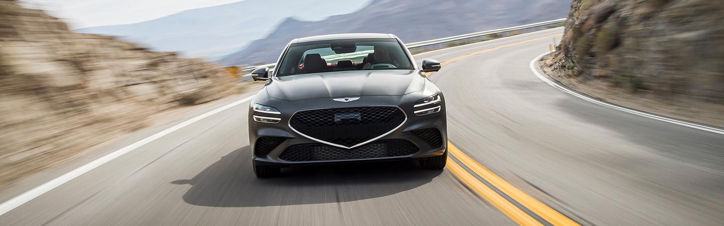 Black 2022 Genesis G70 front view in motion on road in mountain pass