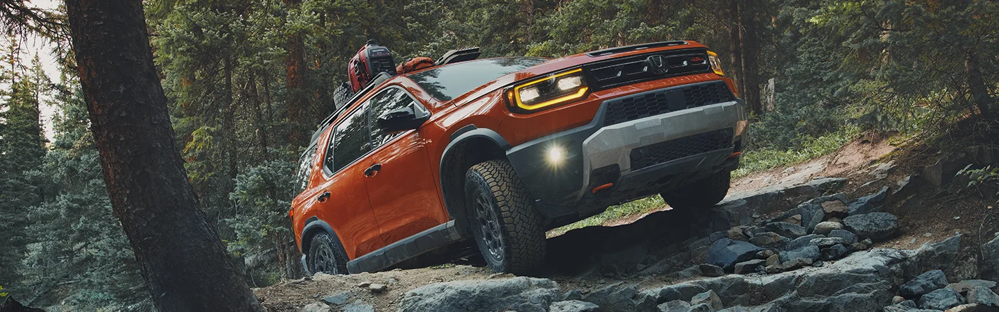 2026 Honda Passport Trailsport Elite Blackout offroad climbing through trees on rocky path