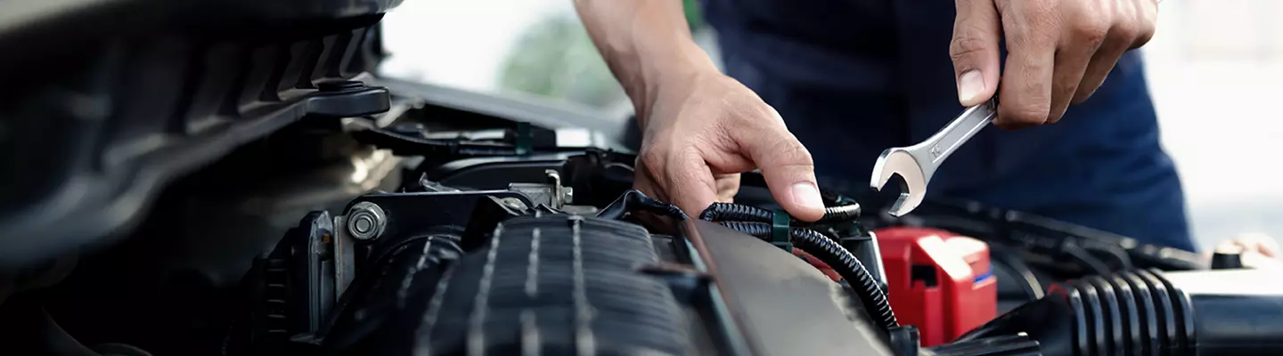 A person using a wrench to repair a car, focused on the engine compartment.  