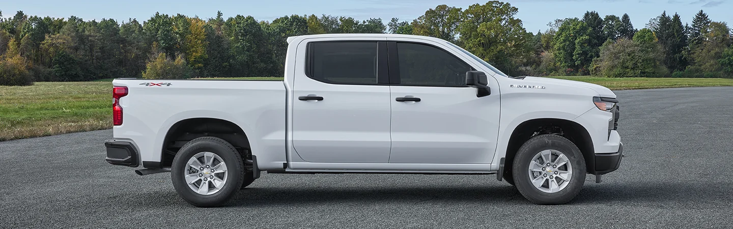 Side view of a white 2025 Chevrolet Silverado 1500 parked by the woods