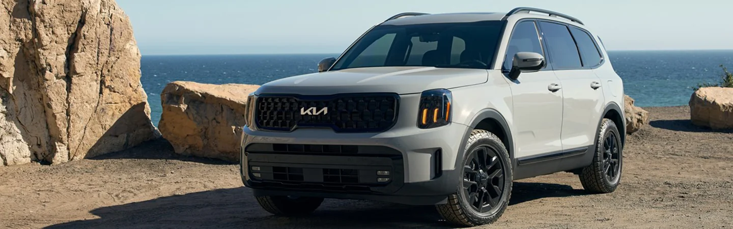 Front side view of a gray 2025 Kia Telluride parked at a rocky side ocean point