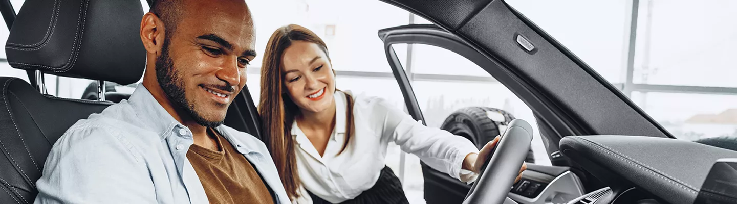 saleswoman leaning into the vehicle smiling and the male driver looking at the wheel