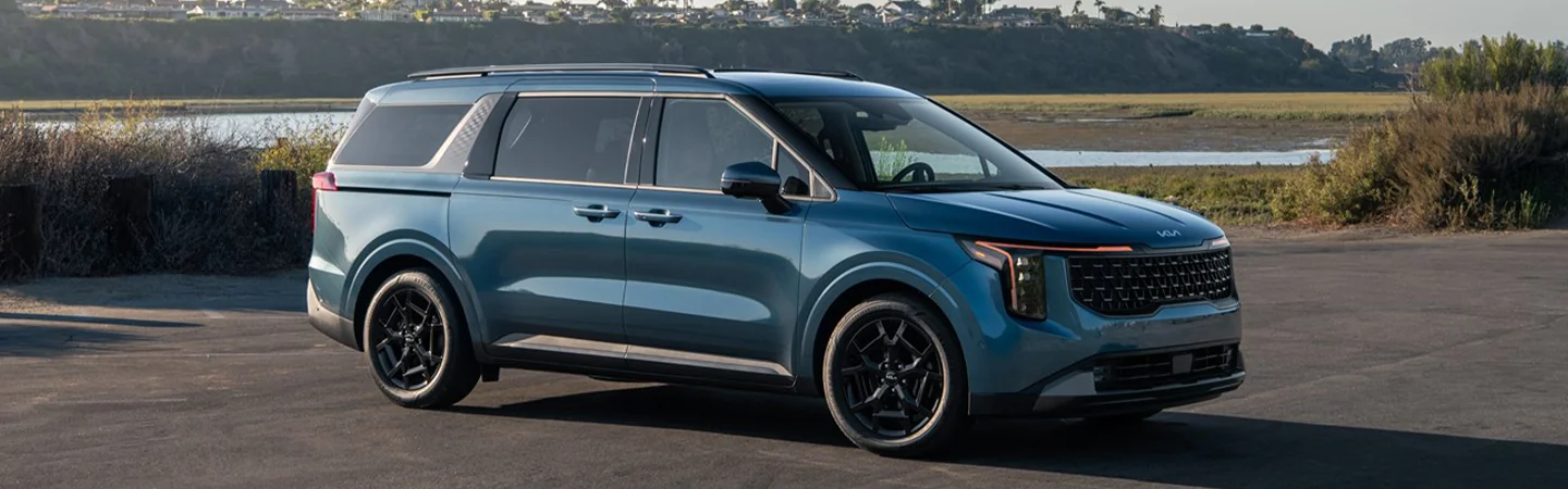 Side view of a parked 2025 Kia Carnival with a lake in the background