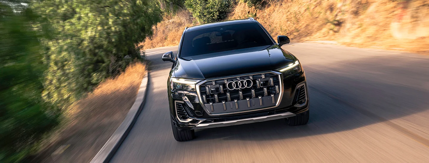 Front view of a black 2025 Audi Q7 driving on a country road