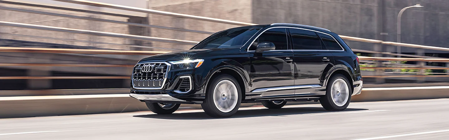 Side view of a black 2025 Audi Q7 driving on a city road