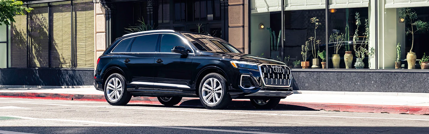 Side view of a parked black 2025 Audi Q7 Specs in front of a city store