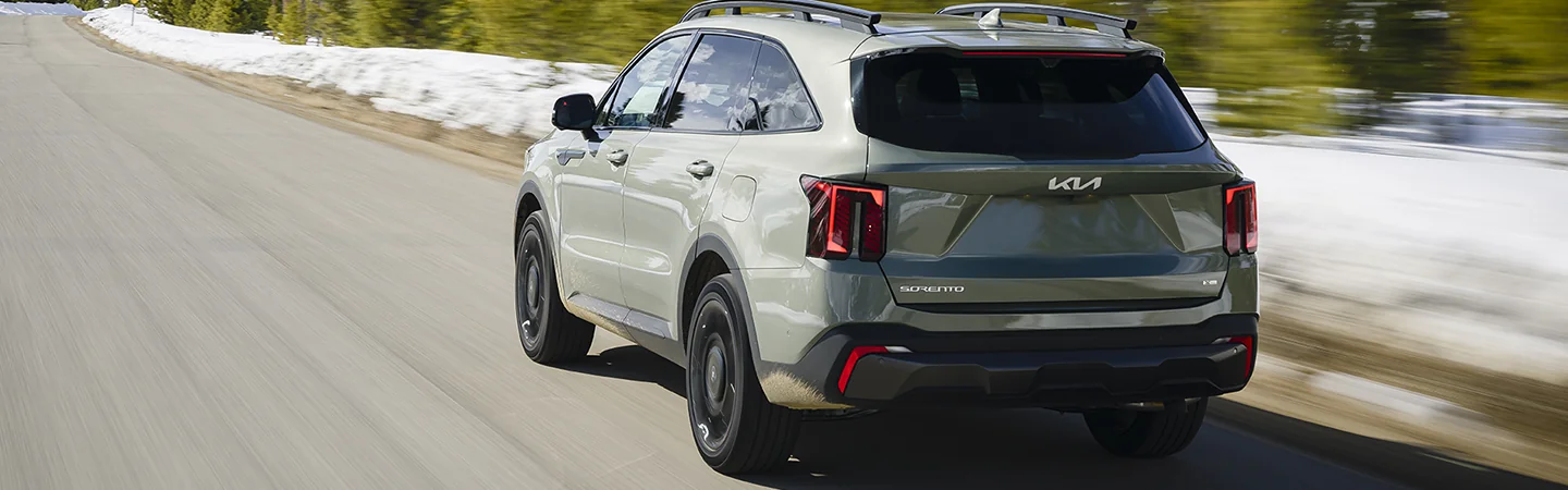Back view of a 2025 Kia Sorento driving on a road next to a snowy forest