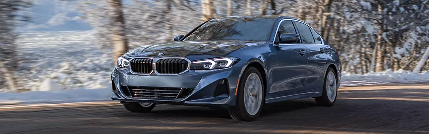 BMW 3 Series driving on a road with snow in the trees