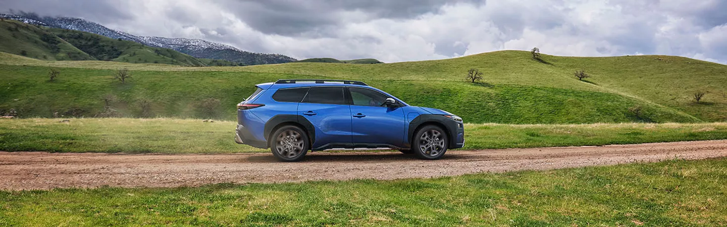 2026 Subaru Trailseeker driving on a road with green hills in the background
