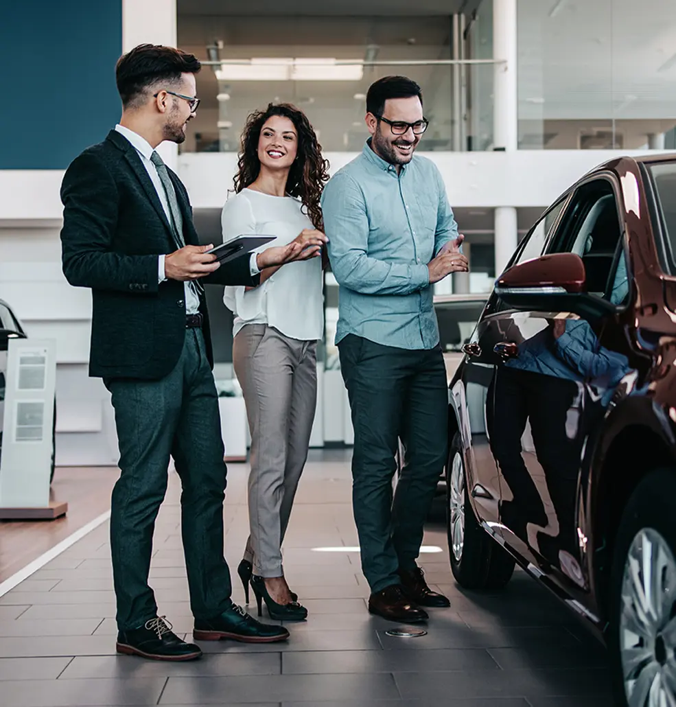 salesman talking with man and woman in the showroom next to a vehicle