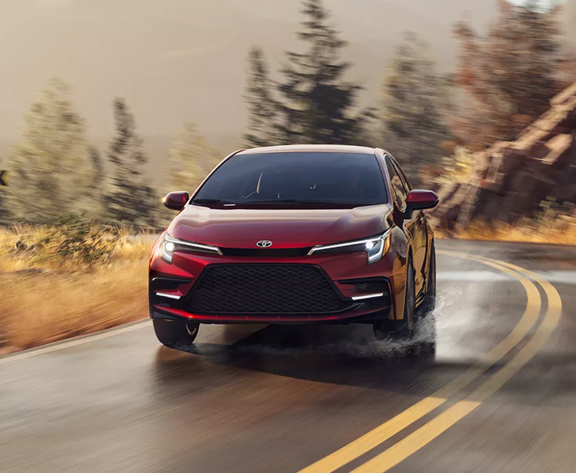 2026 Toyota Corolla driving down the road with a Fall scene behind it